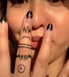 a woman with black and white nail polish holding her hand up to her face while looking at the camera