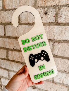 a hand holding up a wooden door hanger with a video game controller on it