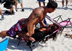 a man and woman laying on top of a chair in the sand at the beach