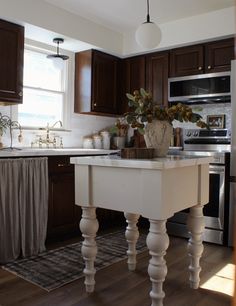 a white kitchen island in the middle of a hardwood floored kitchen with dark wood cabinets