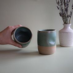 a hand holding a cup next to two vases