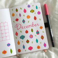 an open notebook with christmas ornaments and the word december written on it next to a pen