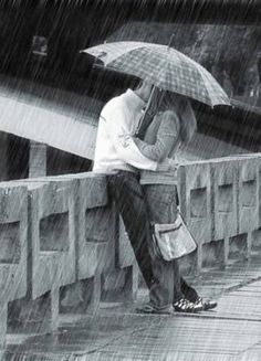 black and white photograph of two people kissing under an umbrella on a bridge in the rain