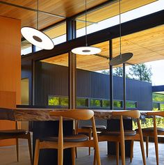 a dining room table with chairs and lights hanging from it's ceiling, in front of large windows