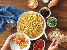 two hands holding plates of pasta with tomatoes, onions and olives on the side