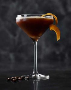 a drink in a glass with an orange peel sticking out of the rim and some coffee beans around it