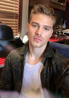 a man in a leather jacket sitting at a table and looking into the camera with an intense look on his face