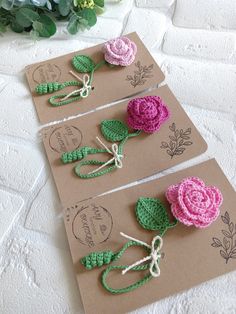 three crocheted flowers are tied to brown cards with green and pink yarn on them