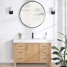 a bathroom vanity with a round mirror above it and plants in the corner next to it