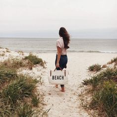 a woman walking down a beach carrying a bag with the word beach written on it