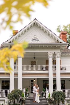 a bride and groom standing in front of a large white house with columns on each side