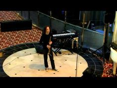 a man standing in front of a microphone on top of a floor next to a piano