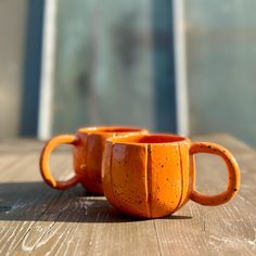 two orange mugs sitting on top of a wooden table