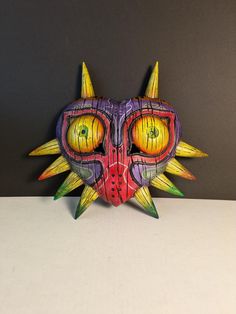 a colorful mask with spikes on it's head and eyes is sitting on a table