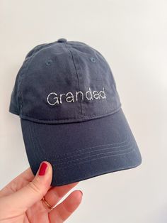 a person holding up a gray hat with the word grandad on it in white letters