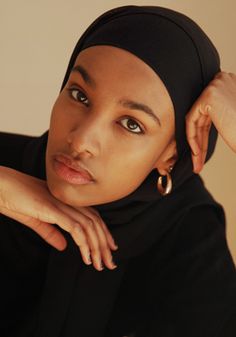 a woman wearing a black hijab and gold hoop earrings is posing for the camera