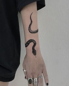 a woman's hand with a snake tattoo on her left arm and two rings around the wrist