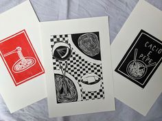 three cards with black and red designs are on a white sheet, one has an image of noodles