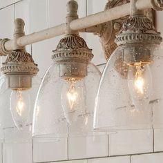 three clear glass globe lights hanging from a white brick wall in an old - fashioned bathroom