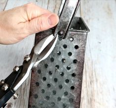 a person holding scissors in their hand over a grate with holes and rivets