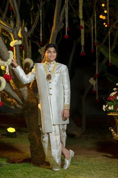 a man standing in front of a tree wearing a white suit with gold trims