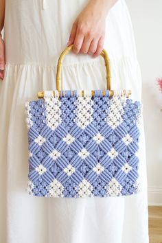 a woman holding a blue and white crocheted purse with gold handles, in front of a wall