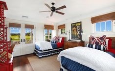 a bedroom with two beds and a ceiling fan in the corner, along with large windows