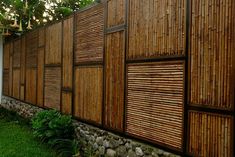 a fence made out of bamboo sticks next to a white wall and green grass in front of it