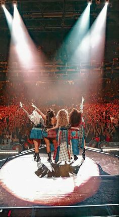 three women in kilts standing on a stage with their arms around each other as the crowd looks on