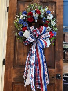 a patriotic wreath hanging on a door with red, white and blue ribbons around it