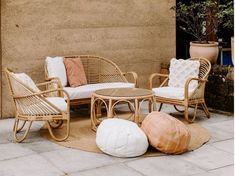 wicker furniture and pillows on the ground in front of a wall with potted plants