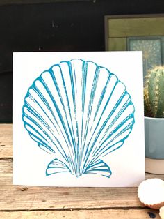 a card with a blue scallop shell on it and a cactus in the background