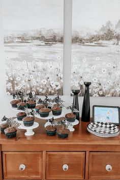 a table topped with lots of cupcakes on top of a wooden dresser next to a painting