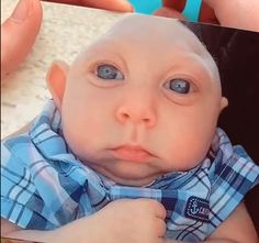 a baby with blue eyes is being held by someone