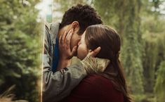 a man and woman kissing each other in front of a mirror with trees behind them