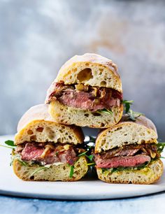 three sandwiches stacked on top of each other with meat and vegetables in the middle, sitting on a white plate