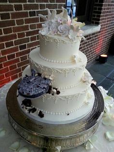 a white wedding cake with flowers on the top is sitting in front of a brick wall