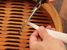 a person cutting paper with scissors on top of a wooden table next to a basket