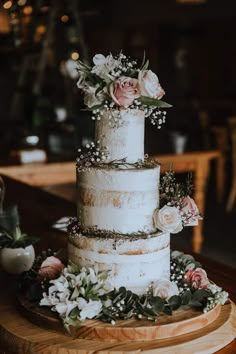 a three tiered cake with flowers and greenery sits on a wooden platter