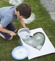 a young boy is painting a heart on the grass