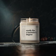 a candle sitting on top of a wooden table next to a black mug with the words smells like a bachelor's degree written on it