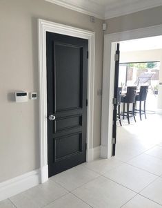 a black door sits in the middle of a white tiled floored entry way to a dining room