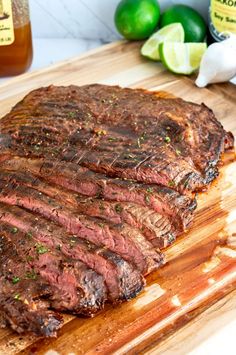 a steak on a cutting board with limes and ketchup in the background