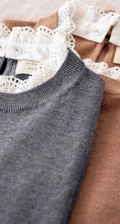 two sweaters with lace on them are laying next to each other, one is brown and the other is gray