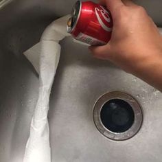 a person is holding a can of soda in their hand and cleaning the sink drain