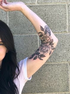 a woman with a flower tattoo on her arm posing for the camera while holding her hand up to her head