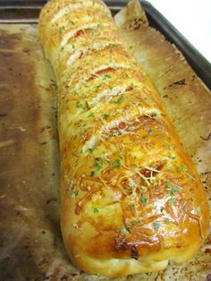 a long piece of bread sitting on top of a baking pan covered in cheese and herbs