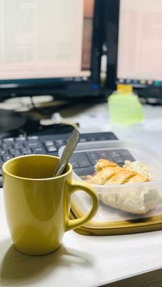 a yellow coffee cup sitting on top of a desk next to a plate with food