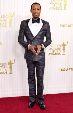 a man in a suit and bow tie standing on a red carpet