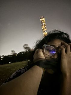 a man is looking through his glasses at the city lights in the distance, while he holds his hand up to his face